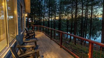 A wooden deck with outdoor seating and a view of a forest and lake.