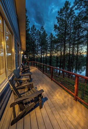 Una terraza de madera con mobiliario exterior y vistas a un bosque y un lago.