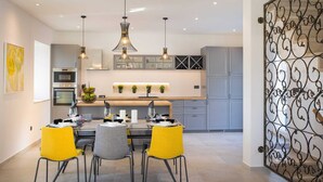 A modern kitchen with grey cabinets, a wooden countertop, and a dining area with yellow chairs.