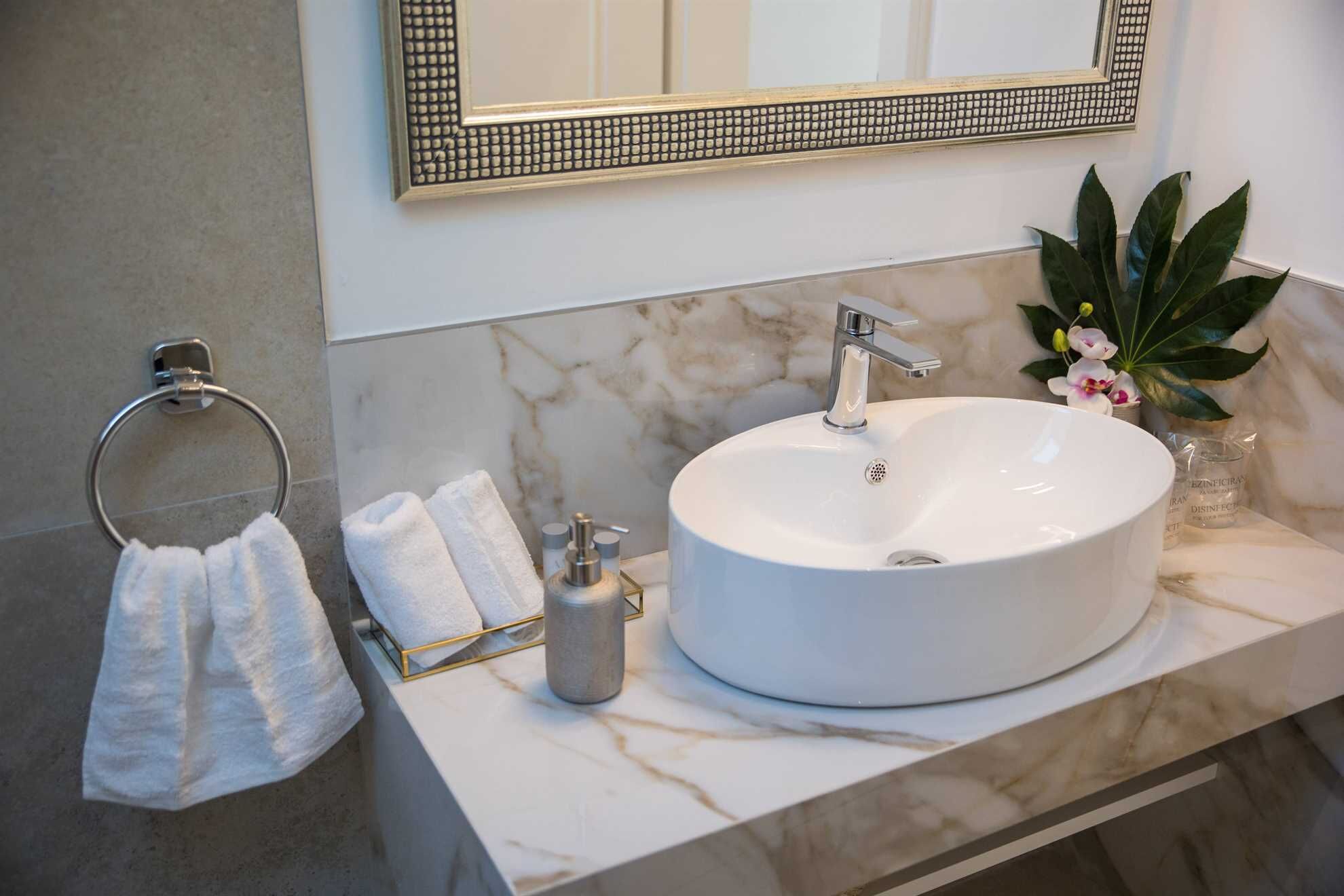 A bathroom with a marble sink, a towel rack, a mirror, and a potted plant.