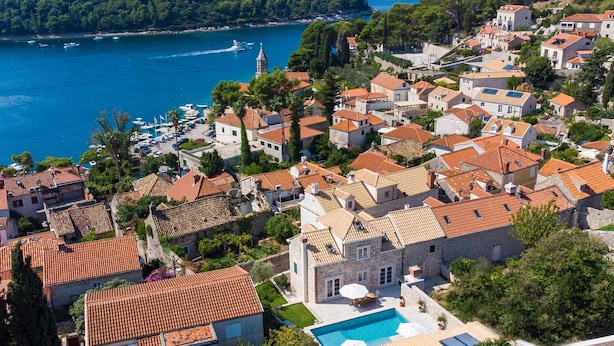 A coastal town with terracotta-roofed buildings, a prominent church, and a swimming pool.