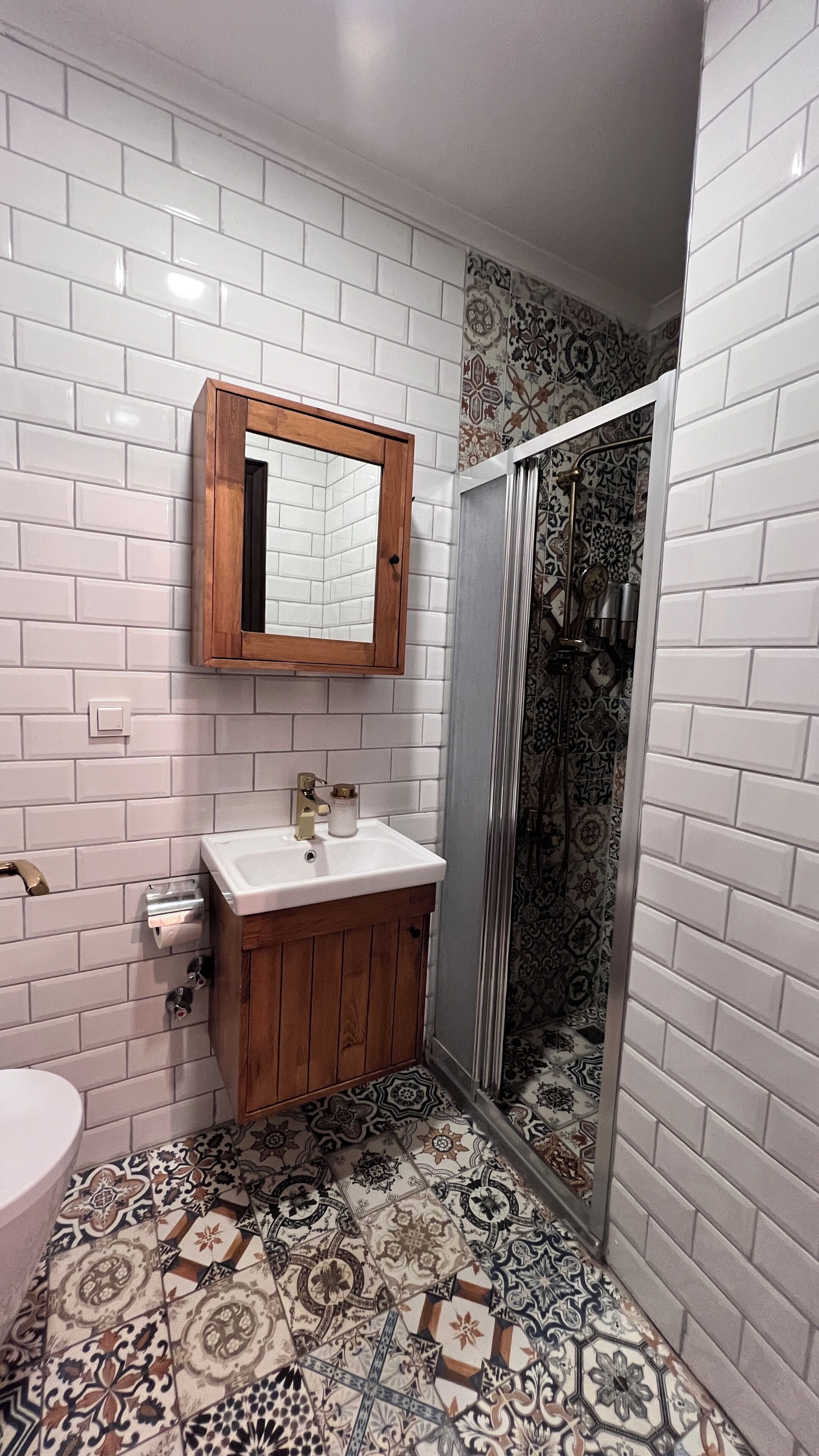 A bathroom with white subway tile walls, a wooden vanity with a sink, and a shower with patterned tiles.