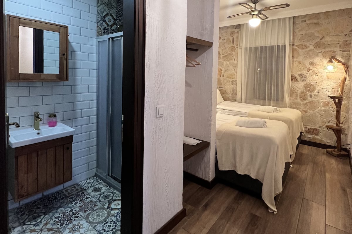 A hotel room with a bathroom, a bed, a mirror, and a ceiling fan.