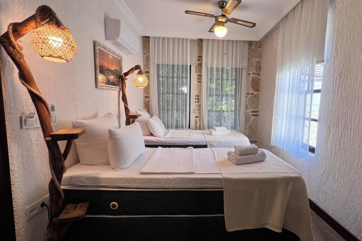 A bedroom with a bed, bedside tables, a ceiling fan, and a view of the outdoors through large windows.