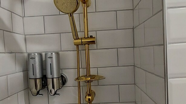 Une douche dotée d’un pommeau de douche doré et d’un pommeau de douche à main, fixés sur un mur carrelé.