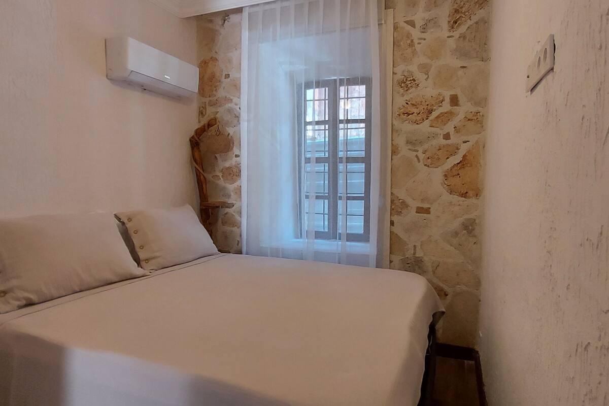 A bedroom with a bed, a window with a view, and a stone wall.