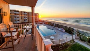 A balcony with wooden chairs and a pool, overlooking a beach at sunset. - Oceanfront views, Beachfront condo, The Driftwood! (north topsail beach)