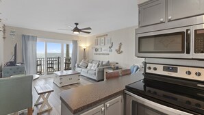 A modern kitchen with a microwave, stove, and cabinets. There is a dining area with a table and chairs, and a balcony with a view. - Oceanfront views, Beachfront condo, The Driftwood! (north topsail beach)