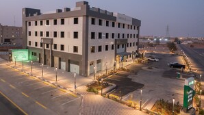 A modern hotel with a parking lot, multiple floors, and a well-lit entrance. - Karims'Hotel (Al Majmaah)