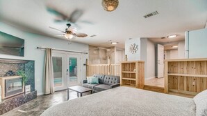 Une chambre d’hôtel moderne dotée d’un grand lit, d’un ventilateur de plafond, d’un coin salon avec un canapé et une table basse, et offrant une vue sur l’extérieur.