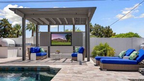 Ein überdachter Außenbereich mit Pool, Fernseher und einer Pergola.