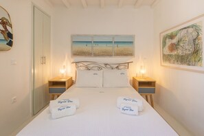 Un lit bien fait, avec deux serviettes, un tableau représentant une scène de plage au-dessus, et une table de chevet en bois avec une lampe de chaque côté.
