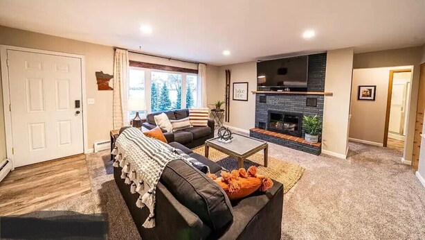 A living room with a fireplace, a sofa, a coffee table, and a door. - Lakefront Condo, 2 bedroom, with Dock & Private Patio! Walk to Restaurants! (Detroit Lakes)