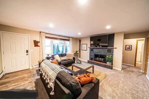 A living room with a fireplace, a sofa, a coffee table, and a door. - Lakefront Condo, 2 bedroom, with Dock & Private Patio! Walk to Restaurants! (Detroit Lakes)