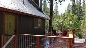 A cabin with a wooden deck, a yellow door, and two red Adirondack chairs.
