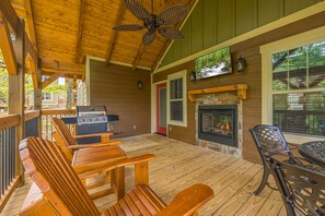 Une terrasse extérieure couverte, aménagée avec des meubles en bois, un barbecue, une cheminée et un ventilateur de plafond.