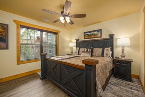 Une chambre à coucher avec un lit en bois, un ventilateur de plafond, une table de chevet avec une lampe et une fenêtre avec des stores.