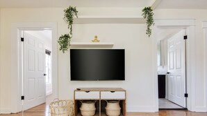 A hallway with a flat-screen TV mounted on the wall, wooden console with drawers, wicker baskets, and white doors.