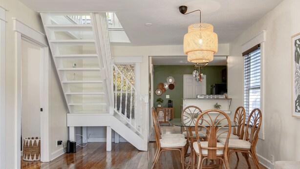 A dining area with a staircase, wicker chairs, and a hanging light fixture.
