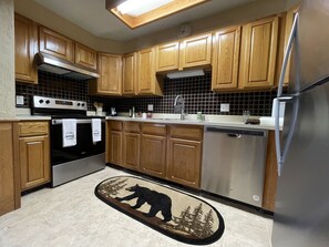 A kitchen with wooden cabinets, a stainless steel refrigerator, and a bear-themed rug.