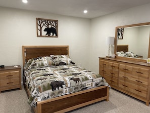 A bedroom with a wooden bed, a nightstand, a dresser, and a mirror.