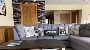 Een gezellige woonkamer met een modulaire bank, decoratieve kussens, een houten salontafel en een bakstenen muur met een houten deur.