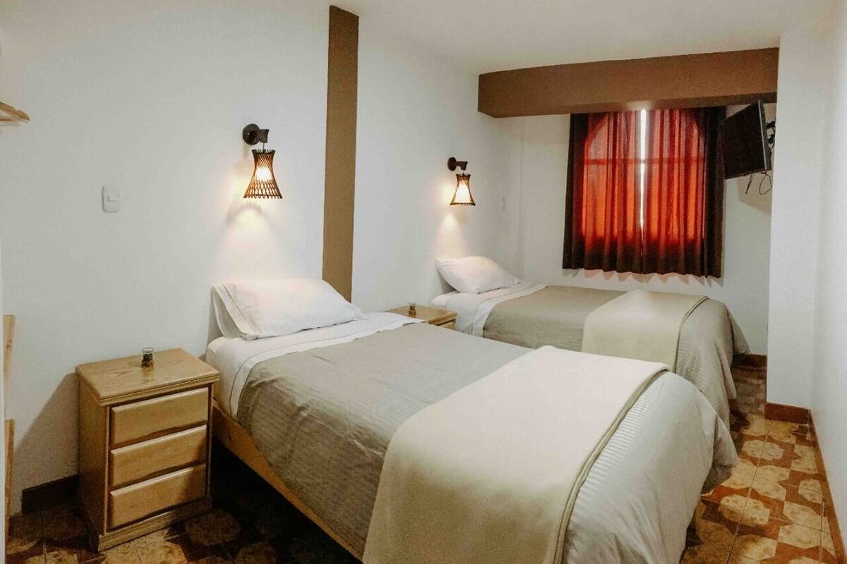 Quarto com duas camas, uma mesa de cabeceira de madeira e uma janela com cortinas vermelhas.