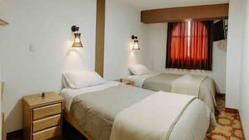 Una habitación con dos camas, una mesita de noche de madera y una ventana con cortinas rojas.