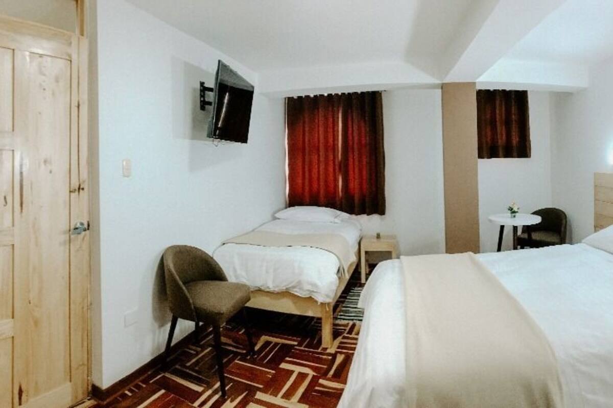 Quarto de hotel com cama, escrivaninha, cadeira, televisão e guarda-roupa.
