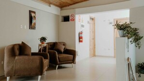 Un interior moderno con dos sillones marrones, una mesita con una planta y un extintor en la pared.