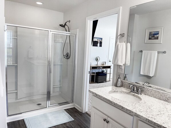 A modern bathroom with a glass shower enclosure, a large vanity with a sink and mirror, and a towel rack. - Beautiful Beach House! Steps away from the Beach! (Port St. Joe)