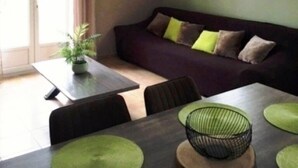 Un espacio de sala acogedor con sofá, una mesa de comedor con individuales verdes, un reloj en la pared y una ventana.