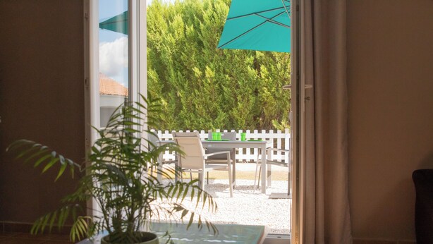Habitación con planta en maceta, una mesa de vidrio y vistas a un patio exterior con valla blanca y sillas.