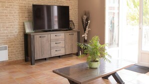 Una sala de estar con una televisión de pantalla plana sobre un mueble de madera, una planta en maceta y un ventanal corredero que da a un espacio exterior.