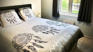 Un dormitorio con cama, dos almohadas, una ventana con cortinas y vistas a zonas verdes.