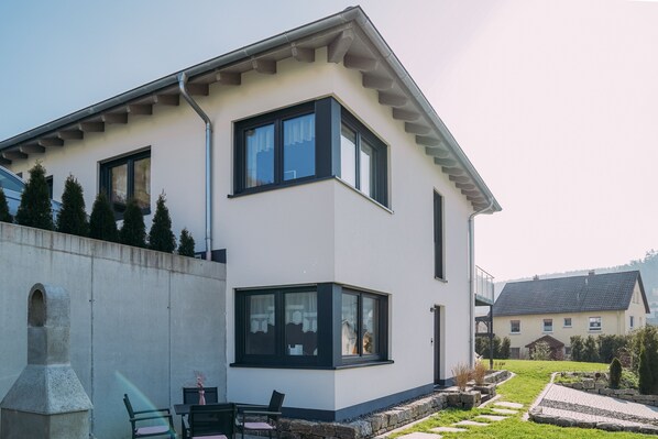 Una casa moderna a due piani con tetto piatto, ampie finestre e un camino in pietra.
