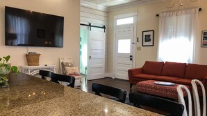 Una sala de estar con un sofá rojo, un televisor montado en la pared y un comedor con una mesa de granito.