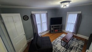 A living room with a sofa, TV, and a fireplace. - The Wesley - Historic 1890 Victorian, Second Floor (Albion)