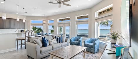 A spacious living room with a large window, a ceiling fan, and a kitchen area with a bar.