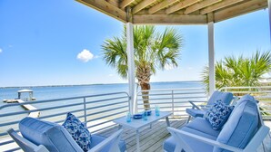 Een houten terras met witte stoelen en een tafel, met uitzicht op een heldere blauwe zee.