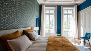 A bedroom with a bed, pillows, a chair, and a window with a view of greenery.