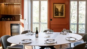 A dining area with a round table set for six, a wine bottle, and a painting on the wall.