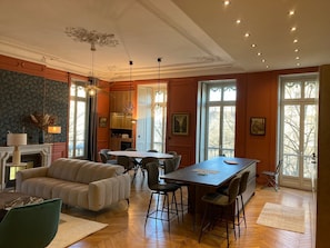 Un salón amplio con chimenea, un comedor con mesa y sillas, y ventanas grandes que ofrecen vistas al exterior.