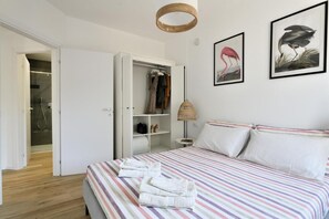 A bedroom with a striped bedspread, a wardrobe, a hanging lamp, and two framed pictures on the wall. - Naked House, Sardinia (Torre di Bari)