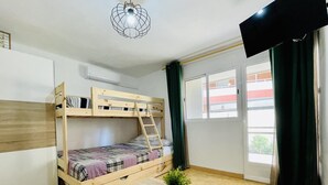 A dorm-style room with bunk beds, a desk, a potted plant, and a window with curtains. - ANAFI - Studio located just 200m from the beach (SALOU)