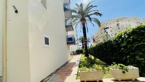 A narrow pathway flanked by buildings, a palm tree, and a hedge. - ANAFI - Studio located just 200m from the beach (SALOU)