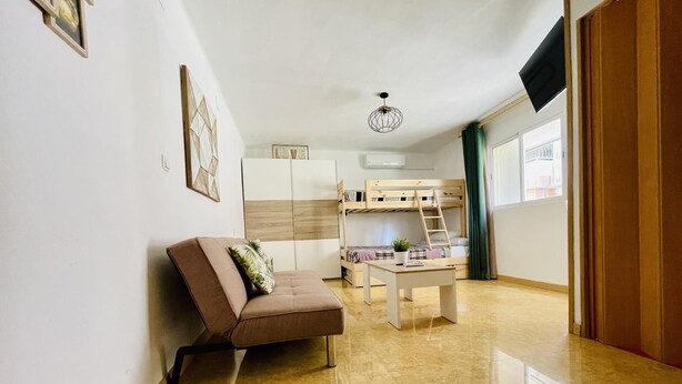 A compact living space with a sofa, a small table, a bunk bed, and a ceiling light. - ANAFI - Studio located just 200m from the beach (SALOU)