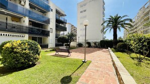 A courtyard with a paved walkway, benches, and well-maintained greenery. - ANAFI - Studio located just 200m from the beach (SALOU)