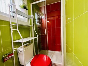 Een badkamer met een rood toilet, een witte wandplank en groene wanden.