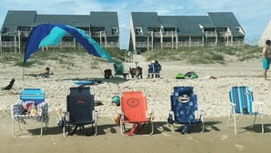A beach with beach chairs, a large blue and teal kite, and a building in the background. - BEACHFRONT:3 BR, 2 Full BA, Renovated, Beach Access , BBQ, Pool, Sleeps 9 (Oak Island)